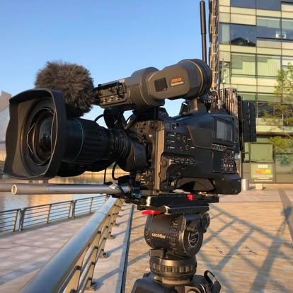 Professional broadcast video camera on a tripod outside a glass building